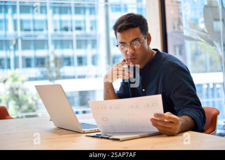 Busy young business man using laptop checking paper working in modern office. Stock Photo