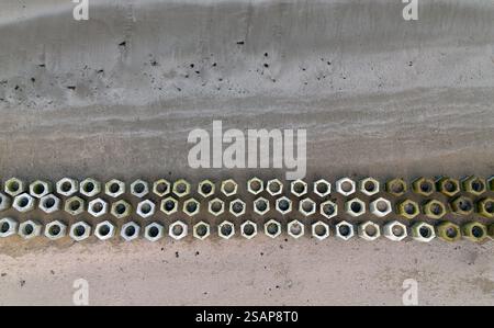 An aerial view on the beach with a three rows of cement blocks on the sand. The nuts are in different sizes and colors. The nuts are arranged in a lin Stock Photo