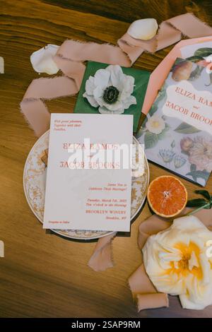 A beautifully arranged wedding invitation set on a wooden table, showcasing delicate floral designs, fresh fruit slices, and soft fabrics that evoke a Stock Photo