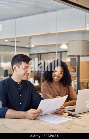 Diverse professional partners using laptop discussing documents in office. Stock Photo
