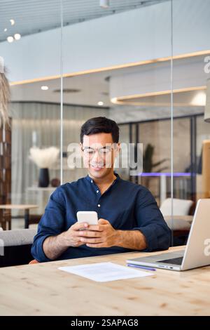 Happy busy Hispanic business man sitting in office using phone. Vertical Stock Photo