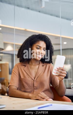 Young happy African American business woman using phone in office. Vertical Stock Photo