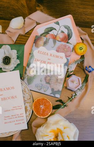 A beautifully arranged wedding invitation suite featuring floral designs, set on a wooden table. Natural elements like dried flowers and citrus fruits Stock Photo