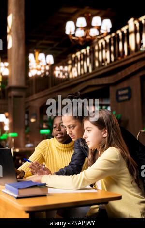 Elementary students receiving support from a tutor working on homework assignments together in a diverse learning environment in the school library. Professor guiding her pupils before class. Stock Photo