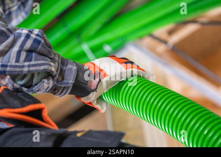 A worker adjusts bright green piping in an industrial space, wearing protective gloves and a plaid shirt, ensuring safety while handling materials. Stock Photo