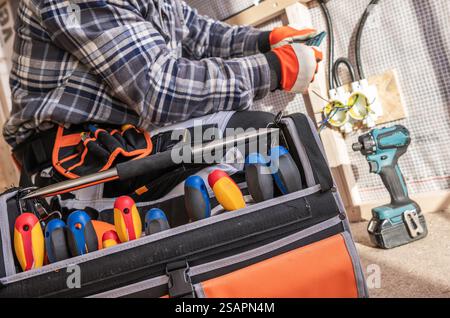 A technician is focused on fixing electrical wiring in a home. He uses various tools from his toolbox, demonstrating skilled work and safety precautio Stock Photo