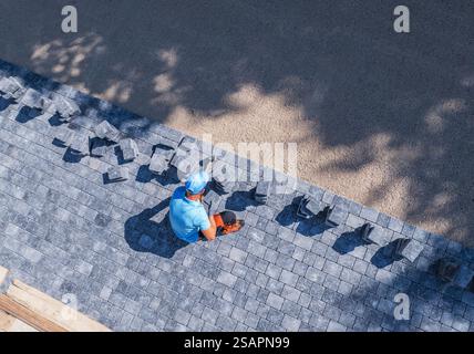 A worker carefully installs gray pavers on a flat surface in bright sunlight, with shadows cast on the ground suggesting a warm afternoon. Stock Photo