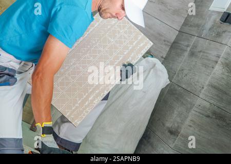 A construction worker installs patterned tiles on the floor of a stylish interior space, showcasing expertise and precision in a well-lit environment. Stock Photo
