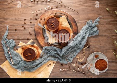 Three chocolate desserts in small bowls, generously dusted with cocoa powder and decorated with chocolate pieces. Set on a rustic wooden table with sp Stock Photo
