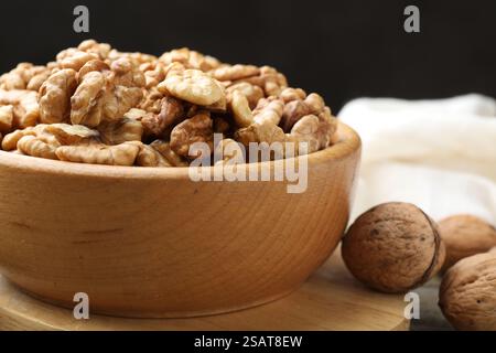 Peeled walnuts in bowl and whole ones on table, closeup Stock Photo
