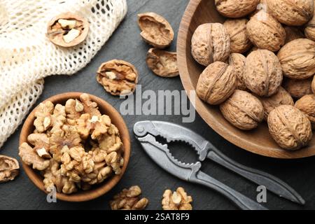 Fresh ripe walnuts, nutcracker and shells on black table, flat lay Stock Photo