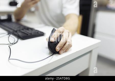 Close-up of a hand operating a mouse on a desk beside a keyboard Stock Photo