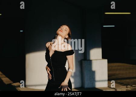 A woman in a black dress with closed eyes expresses joy and freedom in sunlight and shadows Stock Photo