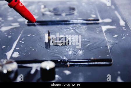 Close-up of a red nozzle spraying water onto a soapy stove surface Stock Photo