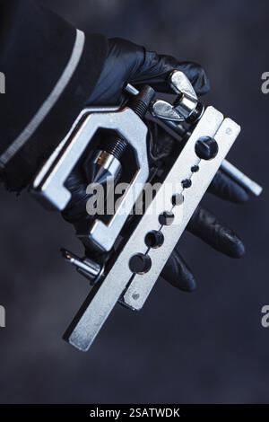 Up-close view of a shiny metal tool held by a gloved hand against a dark backdrop Stock Photo