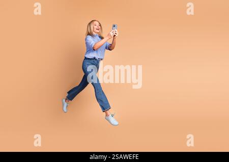 Happy woman in casual outfit enjoys leisure time while taking a selfie against a beige background. Stock Photo