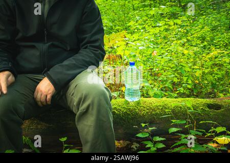 A man sitting on a tree trunk and a plastic bottle of water Stock Photo