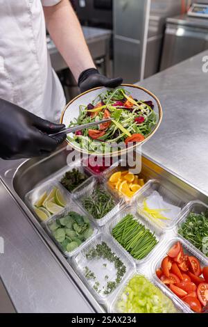 Chef preparing fresh salad in restaurant kitchen using various ingredients Stock Photo