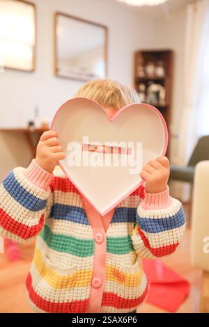 Toddler Holds Up Heart Shaped Box Lid To Face While Nose Peeks Through Stock Photo