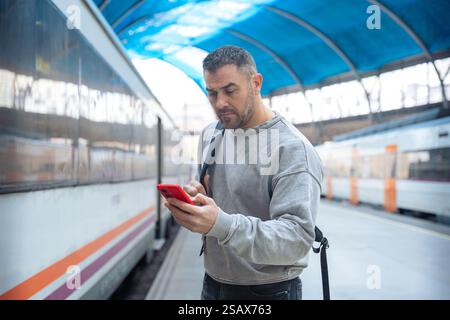 Man Using Red Smartphone at Train Station Stock Photo