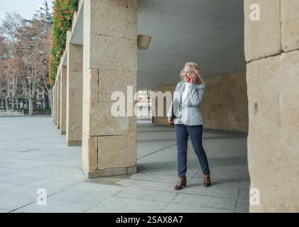 Businesswoman walking and talking on the phone under a portico Stock Photo