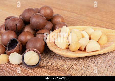 Shelled and unshelled macadamia nuts arranged on a wooden surface, showcasing their creamy interior and dark outer shell. Stock Photo