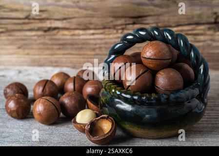A woven basket filled with whole macadamia nuts sits on a rustic wooden surface, with a few nuts scattered nearby, showcasing their rich texture. Stock Photo