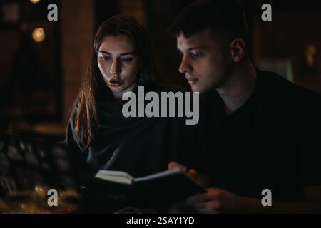 Two individuals reviewing a book together in a dimly lit environment Stock Photo