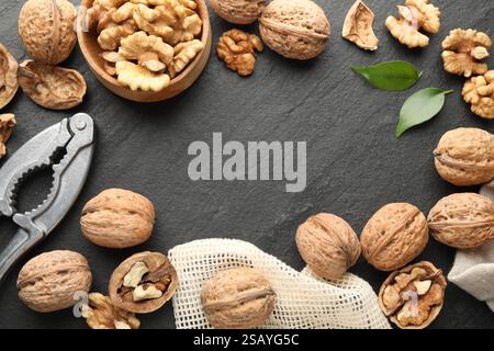 Frame of fresh ripe walnuts, shells and nutcracker on black table, flat lay Stock Photo