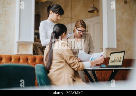 Three female professionals collaborating on a business presentation with charts and reports Stock Photo