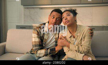 Upset African American married couple sad family renters home owners sit on sofa cuddling worried moving out apartment frustrated woman and man Stock Photo