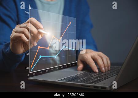 A person is analyzing graphs on a laptop, using virtual elements for interaction. Business finance background Stock Photo