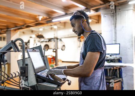 Young mechanic working diligently on a laptop for car diagnostics in a modern, well organized auto repair shop Stock Photo