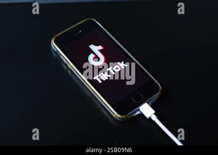 A smartphone placed on a black table showing the TikTok app screen while charging Stock Photo