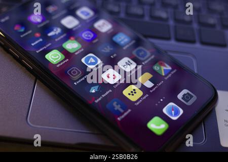 Close-up of a smartphone screen showing various app icons on a laptop keyboard Stock Photo