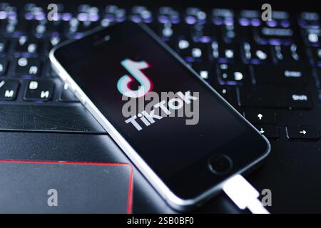 Phone on a laptop, showing the TikTok app logo while connected with a cable Stock Photo