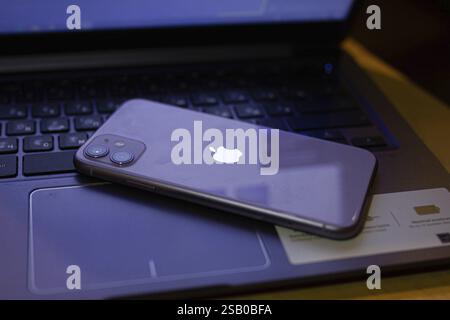 An iPhone placed face down on a laptop keyboard, displaying the Apple logo Stock Photo