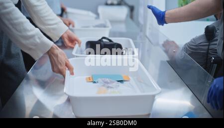 Airport Security Checkpoint during Boarding Flight. Diverse People Put Personal Items in Plastic Trays for Screening: Tablet Computer, Phone, Documents. Security Officers Control Procedures. Close Up. Stock Photo