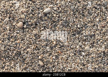 Coastal pebble mixed with coarse sand in a sunlight, top view, close-up background photo texture of a beach ground Stock Photo