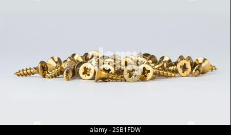 A pile of golden screws lies on a white surface ready for various projects Stock Photo