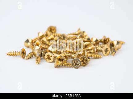 A pile of golden screws lies on a white surface ready for various projects Stock Photo