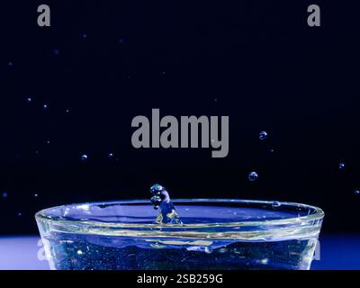 Dynamic capture of crystal-clear water droplets suspended in mid-air above a glass bowl, set against a stark, deep blue backdrop. The image captures t Stock Photo