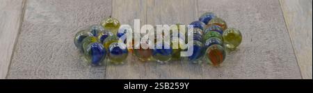 Panoramic view of a vibrant assortment of glass marbles, each uniquely patterned, artfully arranged on a rustic wooden surface that enhances their ric Stock Photo