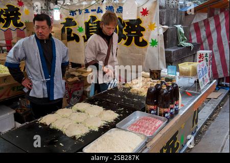 Two men preparing Hiroshima-style okonomiyaki Japanese pizza pies at a festival stall during an event at Kitano Tenmangu shrine, Kyoto, Japan. Stock Photo
