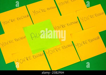 A green sticky note with the word "always" written on it. There are other yellow sticky notes with the word "you're enough" written on them. Concept p Stock Photo