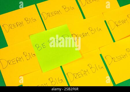 A green sticky note with the words "be bold" written on it. There are several other yellow sticky notes with different words written on them. Concept Stock Photo