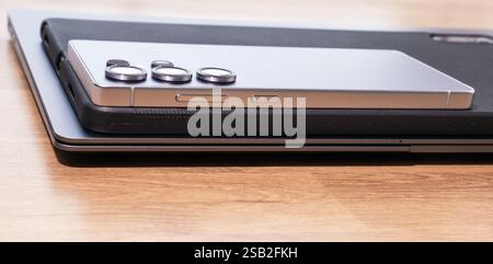 A new silver cell phone and black tablet are placed on top of a silver laptop. The cell phone is positioned slightly above the laptop, with the laptop Stock Photo
