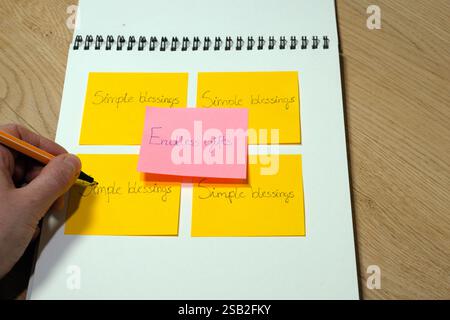 A person is writing on the spiral bound notebook with a pink sticky note on it. The sticky note says "Endless Gifts" and is in the middle of the noteb Stock Photo