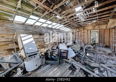 A room with a lot of debris and a refrigerator in the middle. The refrigerator is on the left side of the room Stock Photo