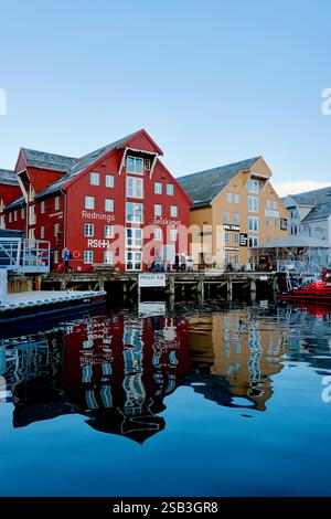 Harbourside buildings in Tromso, Norway, reflect on calm waters at sunset, showcasing colourful architecture and a docked rescue boat Stock Photo